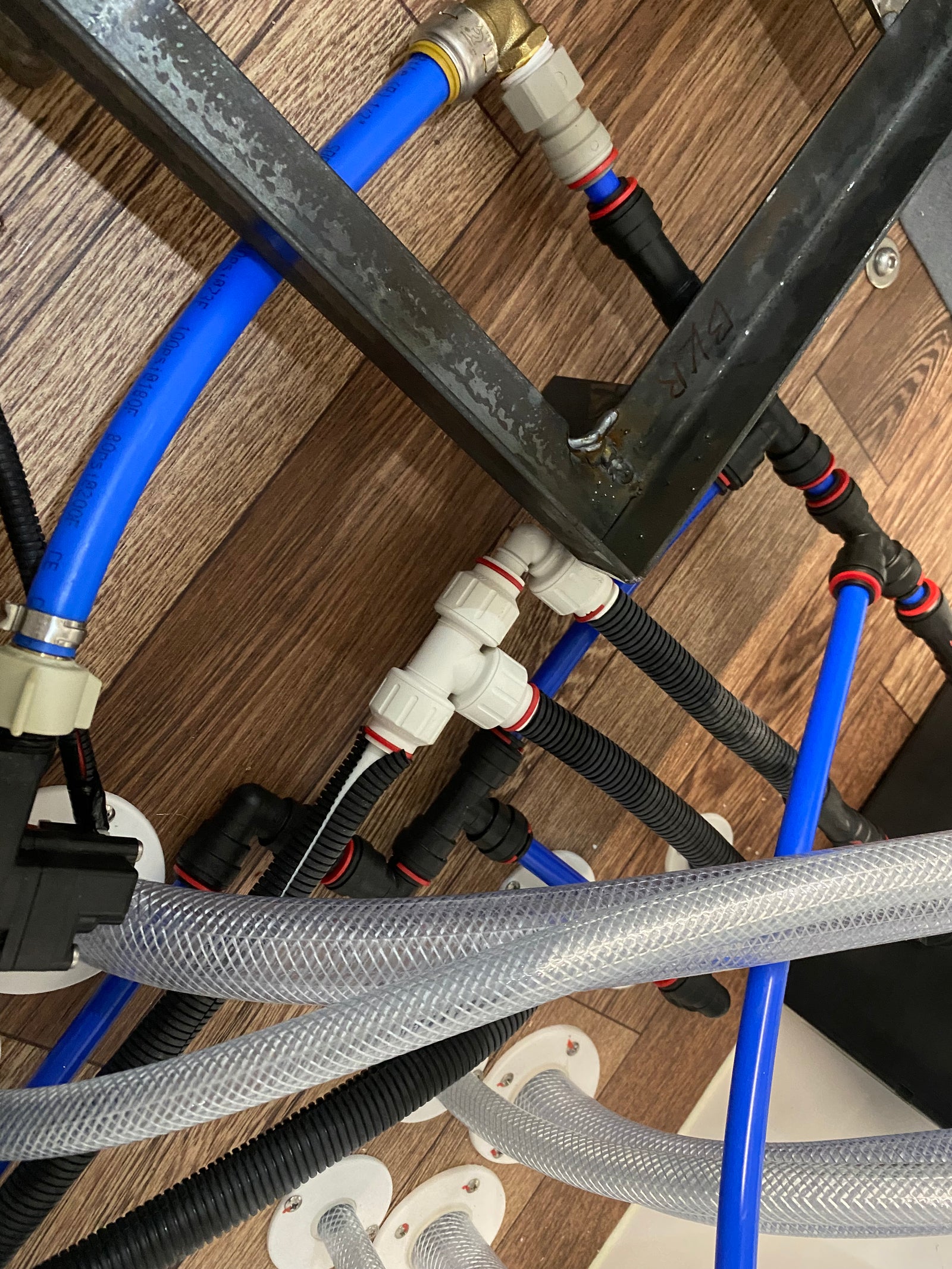 Blue PEX water lines, protected hoses, and serviceable push-fit plumbing connections beneath a vehicle floor