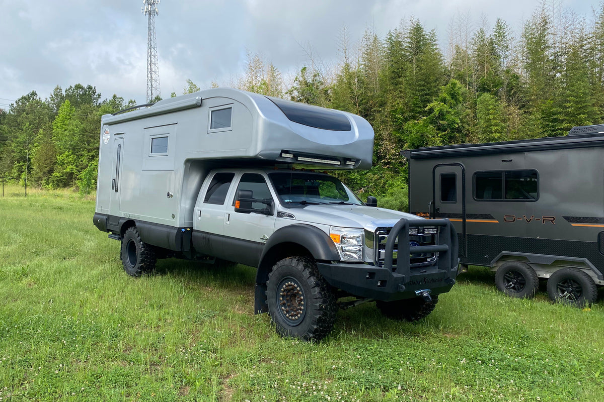 Ford expedition truck with a composite camper body beside an off-road trailer